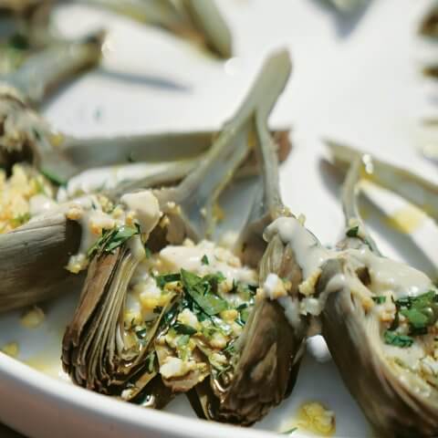 Artichokes sliced in half and arranged in a circle on a white plate