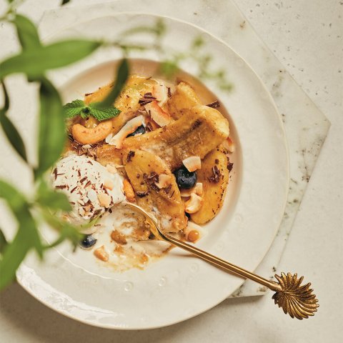 A white dish with a decorative gold spoon and dessert with green leaves in the foreground.