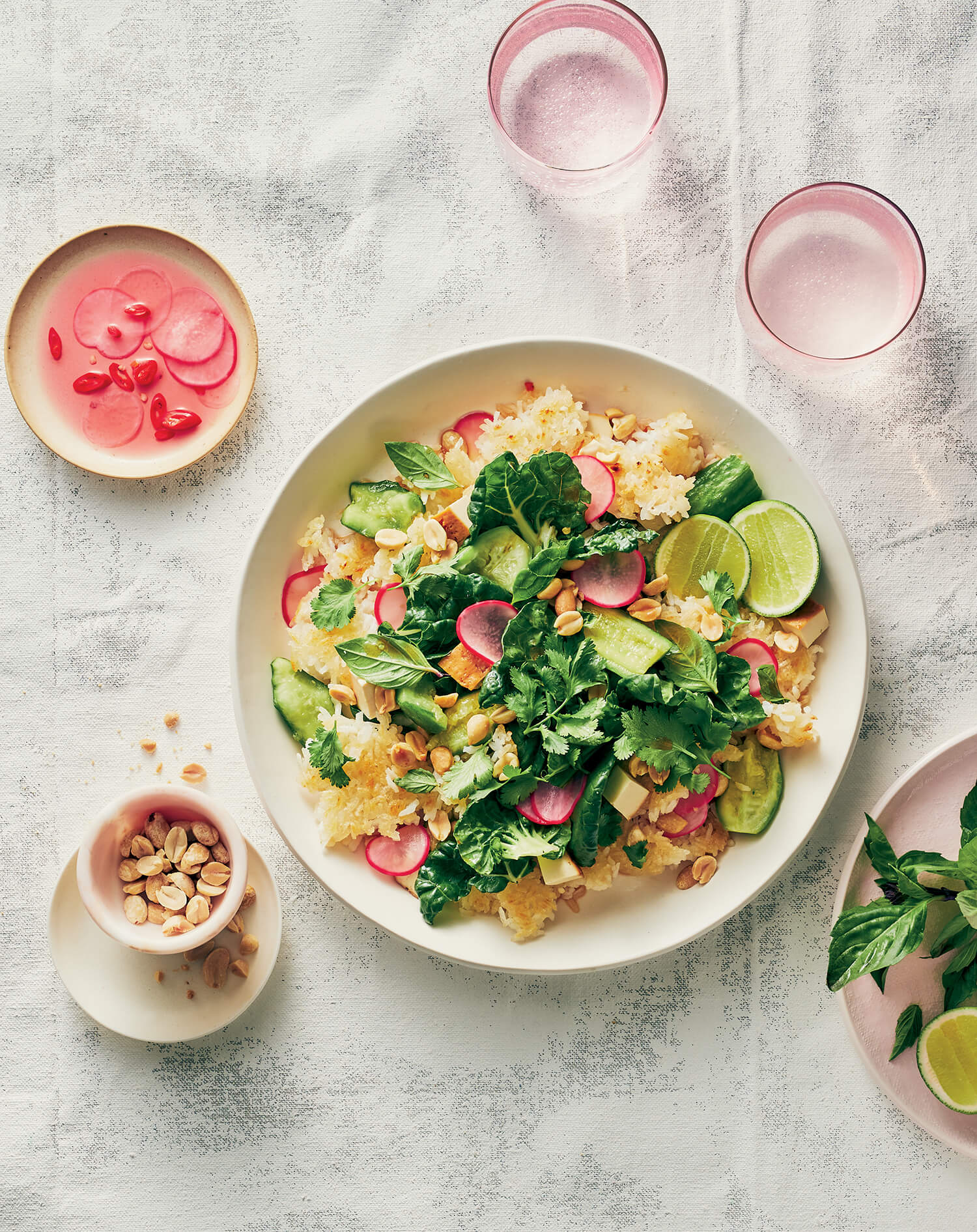 A white plate with salad and pink dishes with drinks and garnishes next to it.