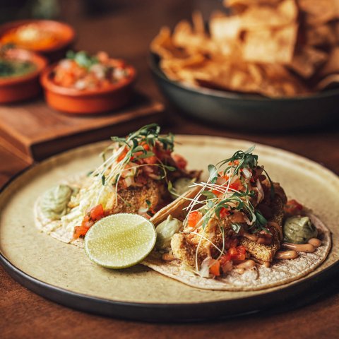 A plate with tacos and sauce dishes on a wooden table