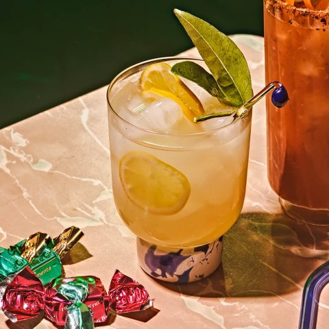 A tumbler glass with lemonade on a marble surface with wrapped candies next to it.