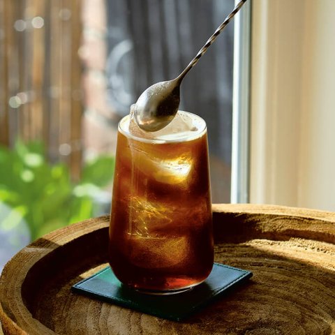 A person's hand stirring a cocktail with a bar spoon.