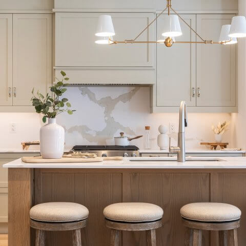 A kitchen island with three stools, dark wood and light green cabinetry.