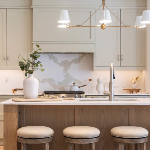 A kitchen island with three stools, dark wood and light green cabinetry.