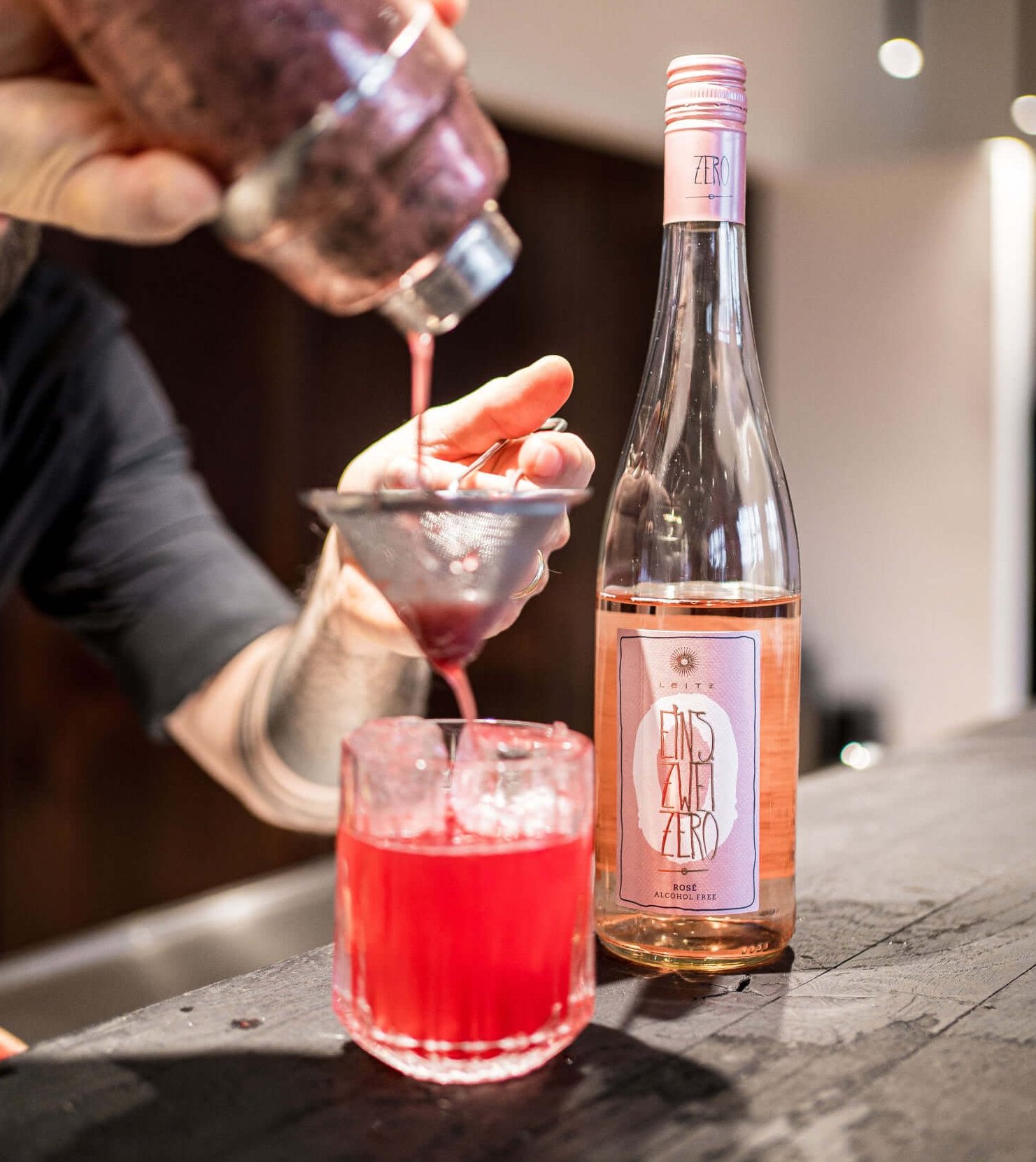 A bartender making a cocktail with a bottle of rosé wine in the background.