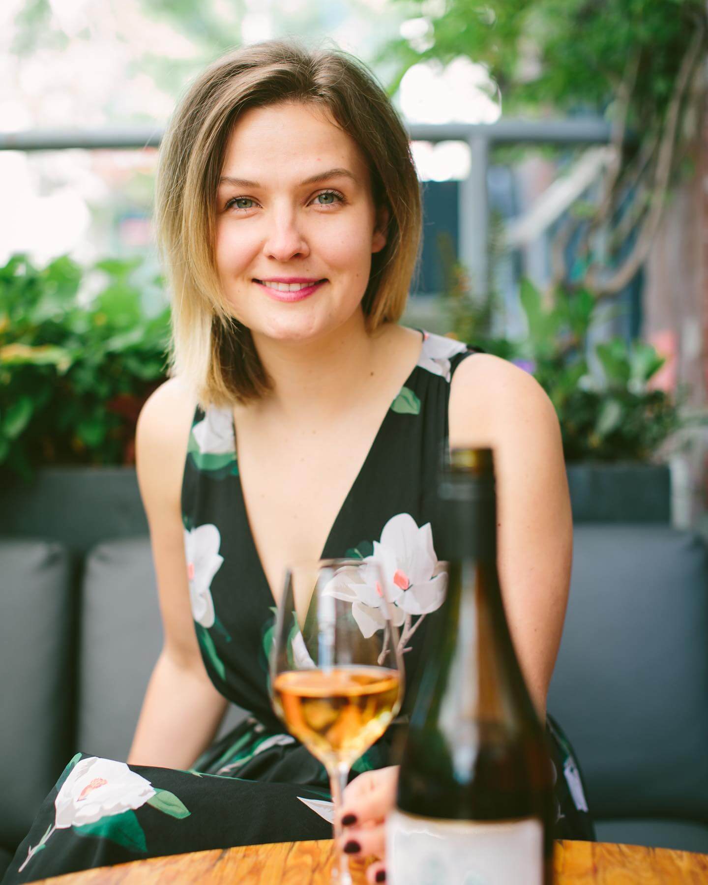 A woman sitting at a table smiling with a glass of wine in front of her.