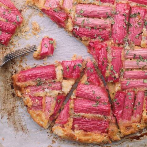 A galette with pieces of rhubarb on top, sliced into pieces with a fork visible.