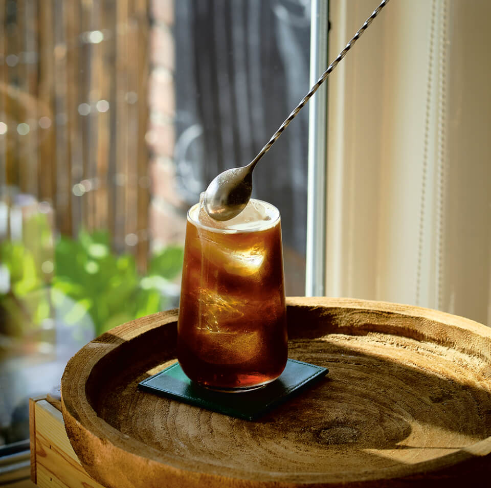 A person's hand stirring an Irish Whiskey boilermaker cocktail with a bar spoon.