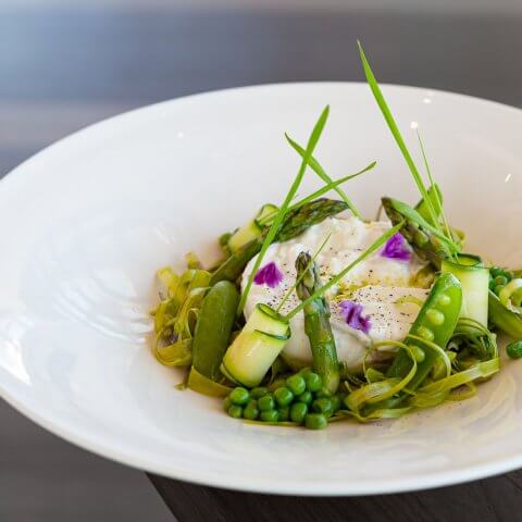 An artfully arranged salad of burrata and green vegetables in a white salad plate.