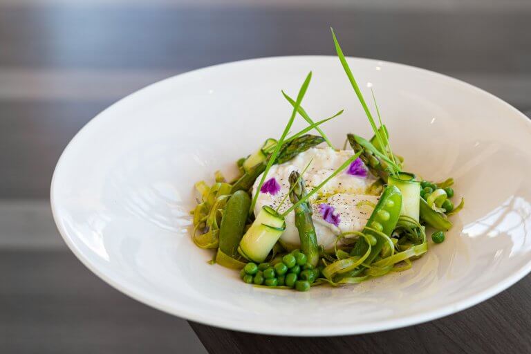 An artfully arranged salad of burrata and green vegetables in a white salad plate.