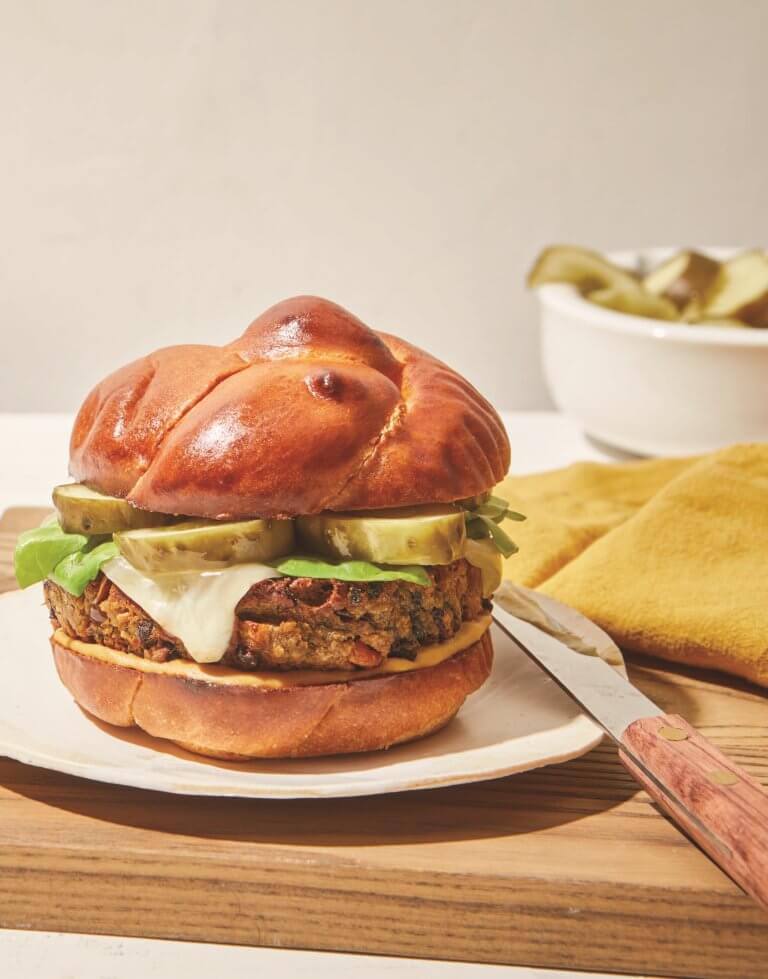 A burger on a plate with a yellow napkin and knife