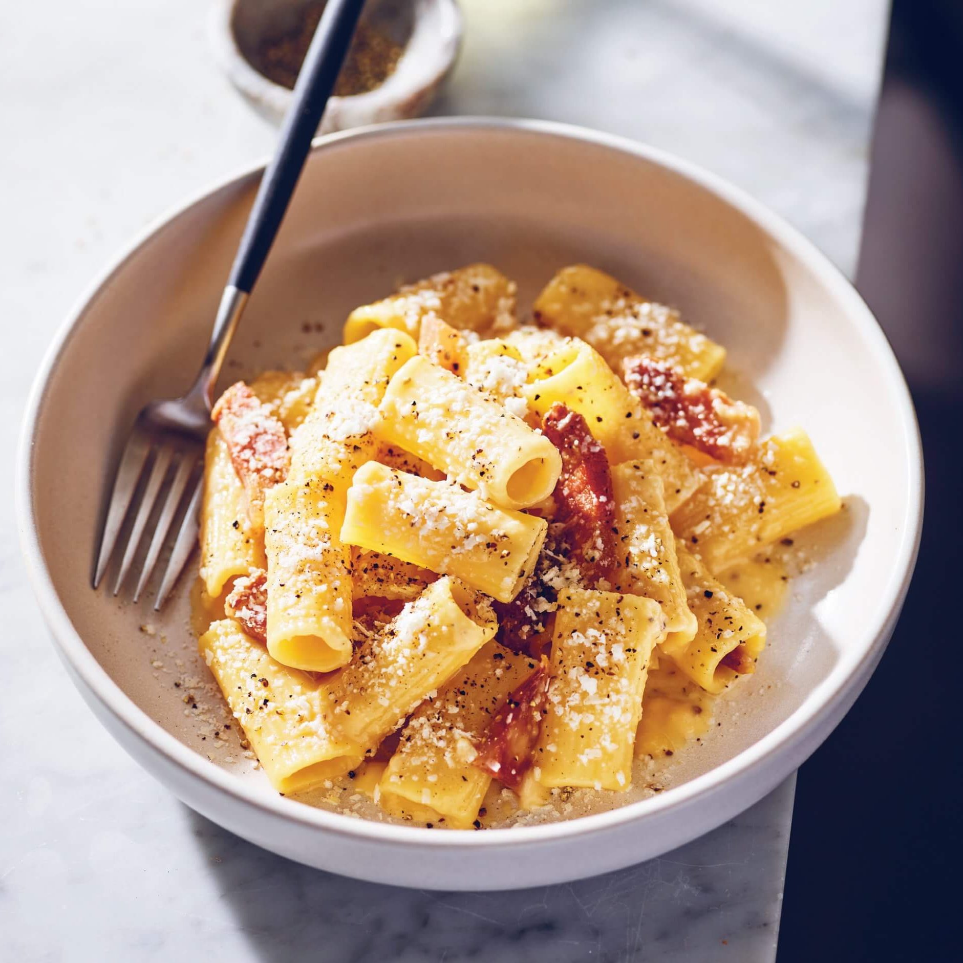A pasta bowl with carbonara and a fork