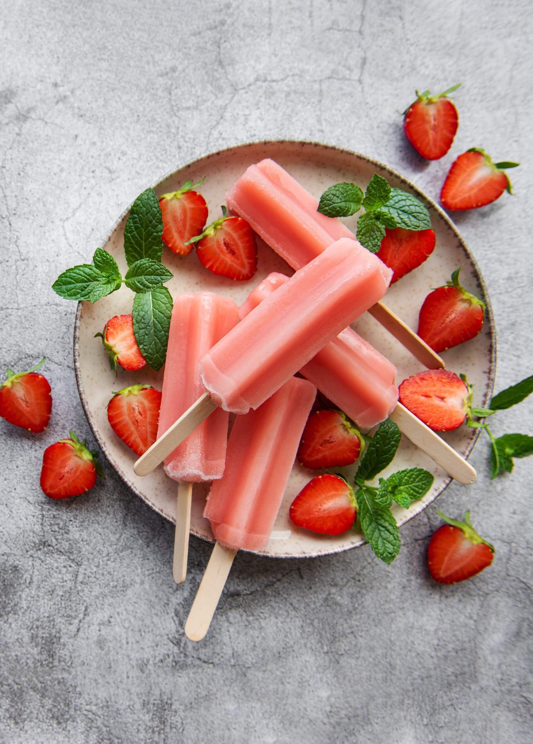 A plate of popsicles surrounded by strawberries and green garnishes