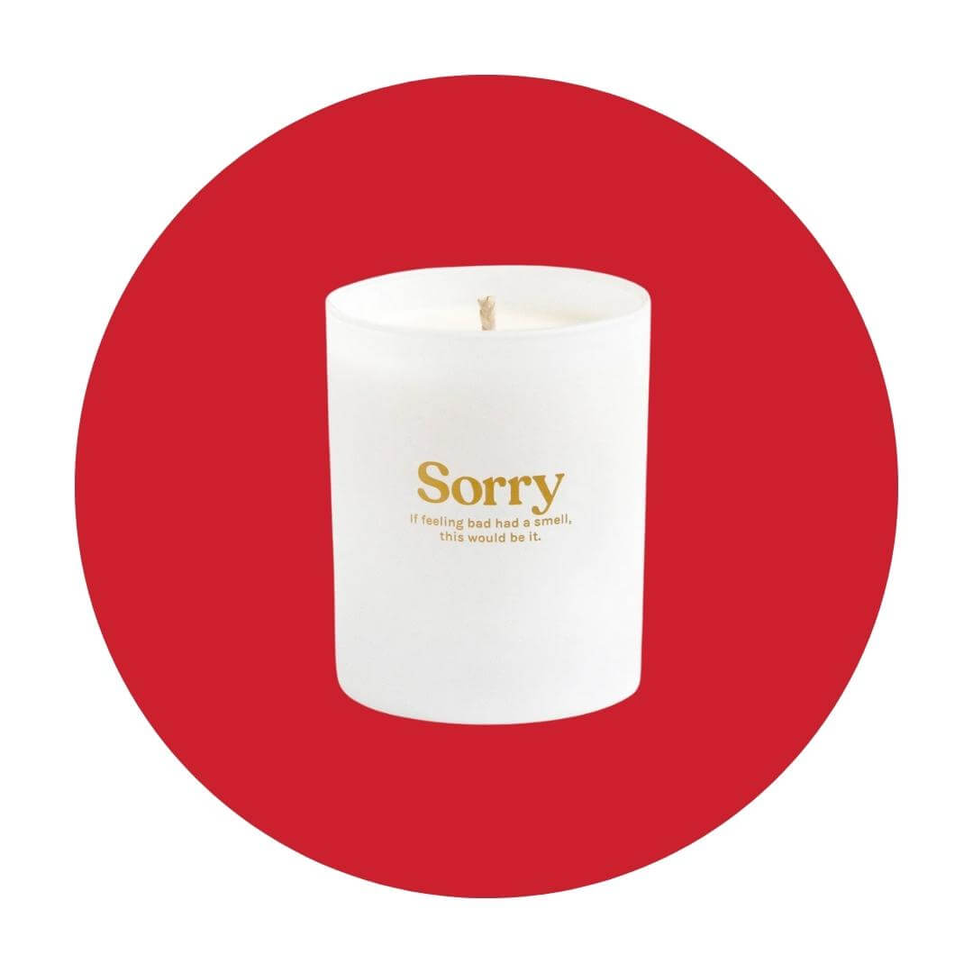 A white candle with gold lettering on a red circle graphic