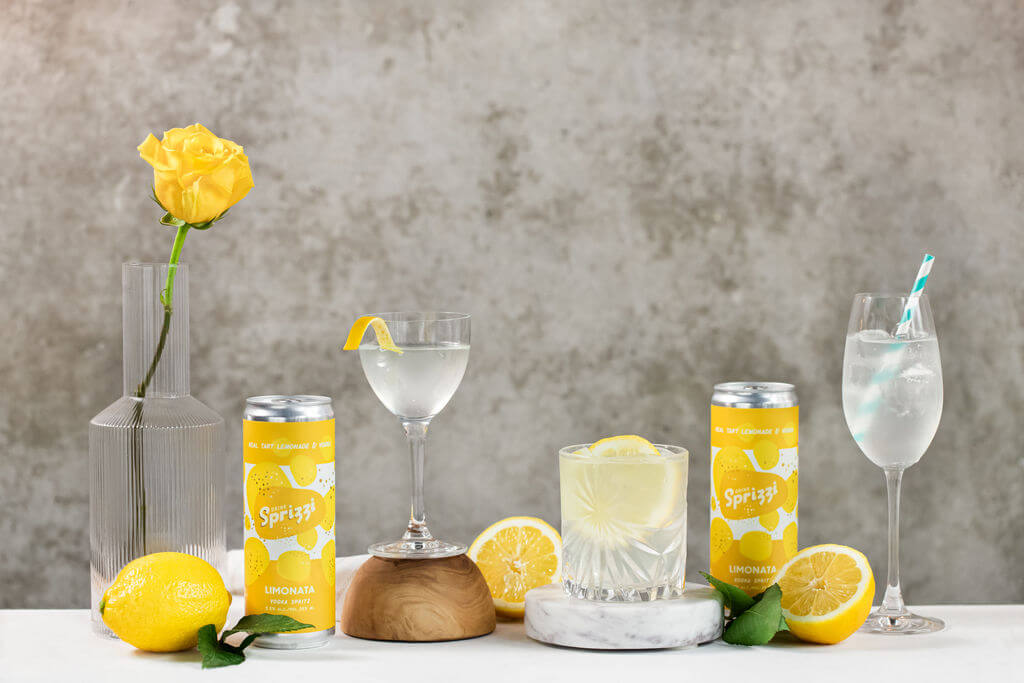 Half a grapefruit surrounded by green leaves and colourful drink cans