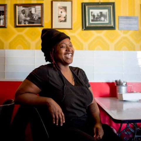 Jamaican-Canadian chef Suzanne Barr sitting at a table in a dining room with yellow walls covered in photos.