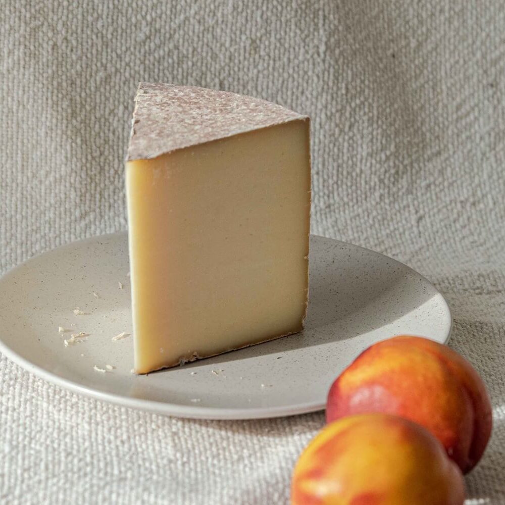 A slice of cheese on a white plate with two peaches in the foreground.