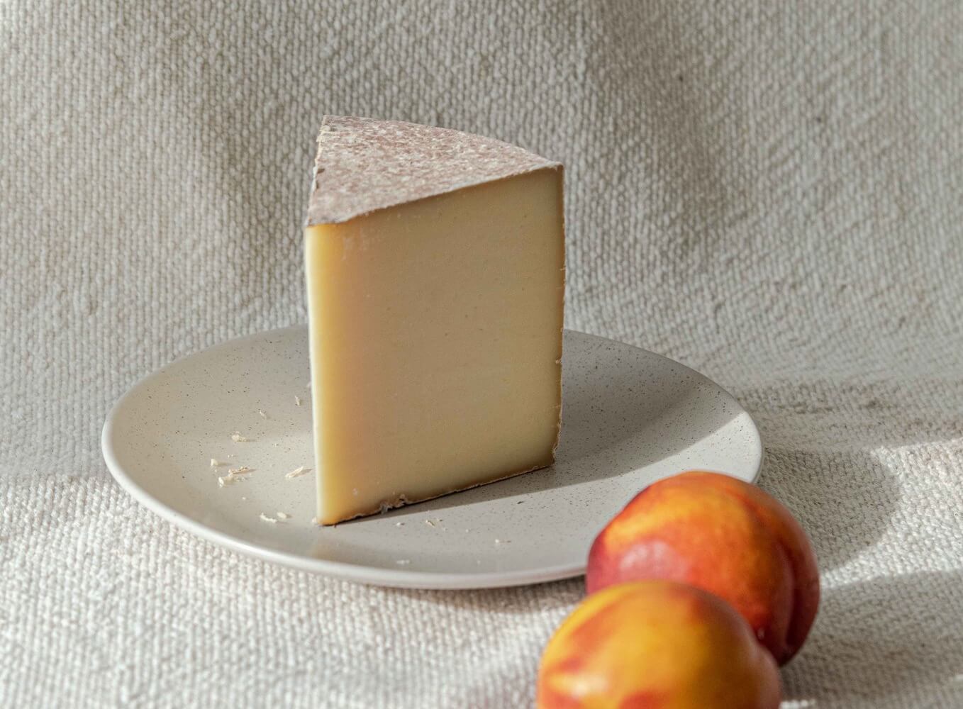 A wedge of cheese on a plate with two pieces of fruit next to it 