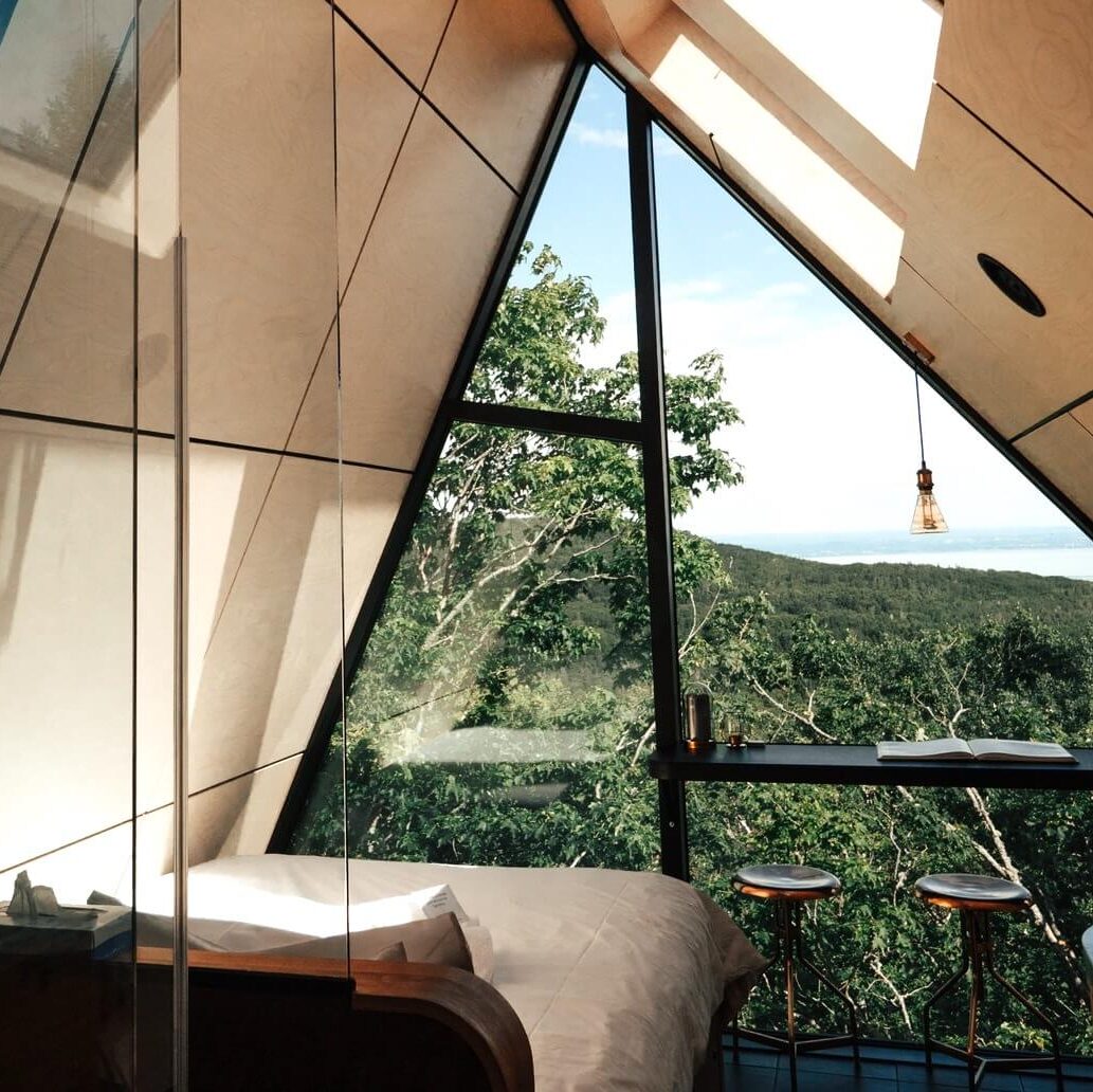 A bed facing a large triangular window overlooking greenery.