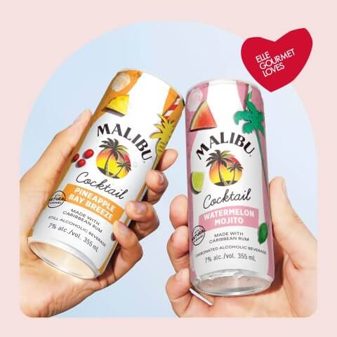 Two hands holding canned cocktails against the sky, in a light pink frame with a heart bearing the words "ELLE Gourmet Loves"