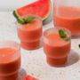 Pitcher of strawberry watermelon smoothie poured into glasses with a fresh watermelon wedge.