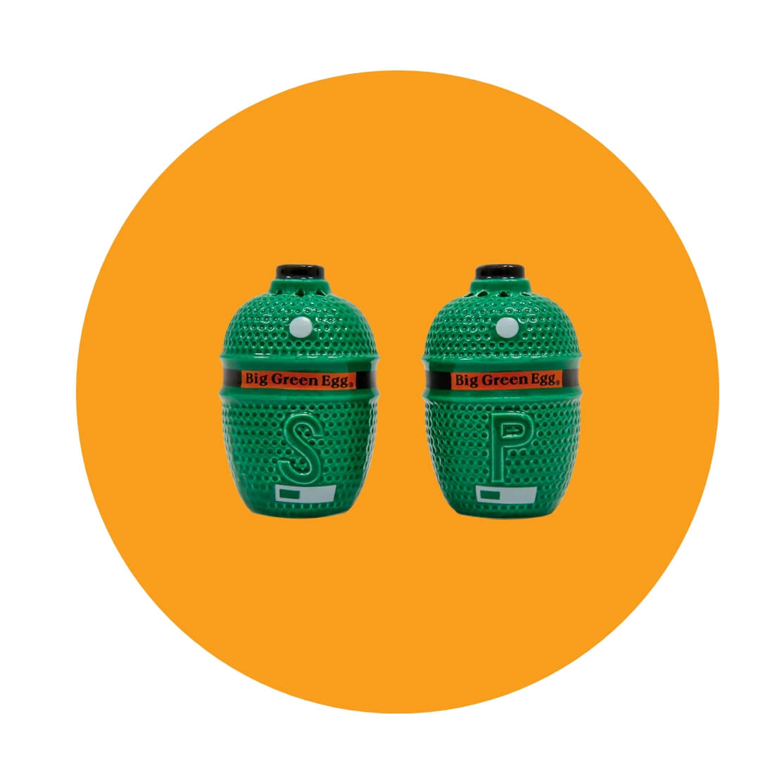 Two salt and pepper shakers shaped like Big Green Egg barbecues on an orange circle graphic