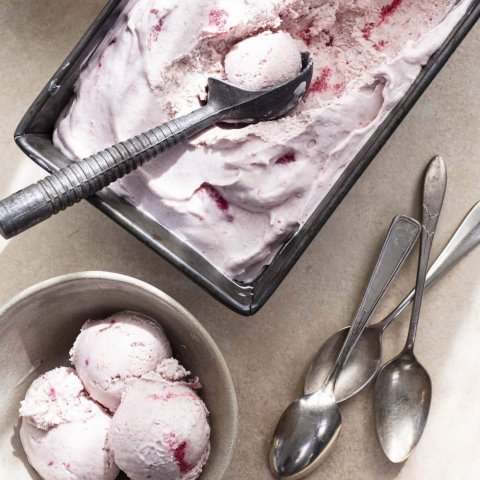 A pink-coloured ice cream in a silver vat with scoops and spoons