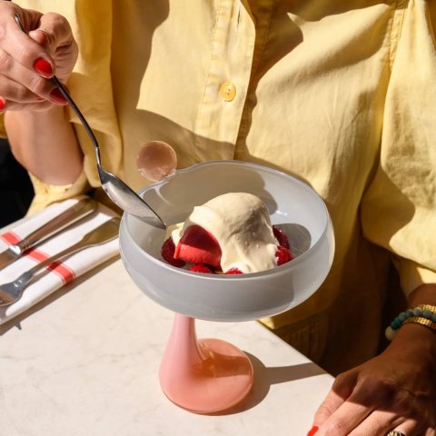 A person in a yellow top eats ice cream from a tall blown-glass in pastel shades