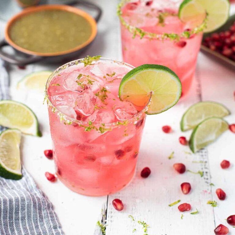 Pink pomegranate margaritas garnished with lime and pomegranate seeds.