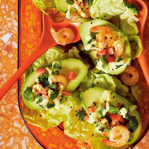 A bright orange dish with avocados stuffed with shrimp and vegetables, with a matching serving spoon, on an orange and white linoleum surface
