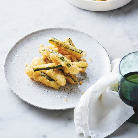 A white dish on a marble background with deep fried zucchini slices