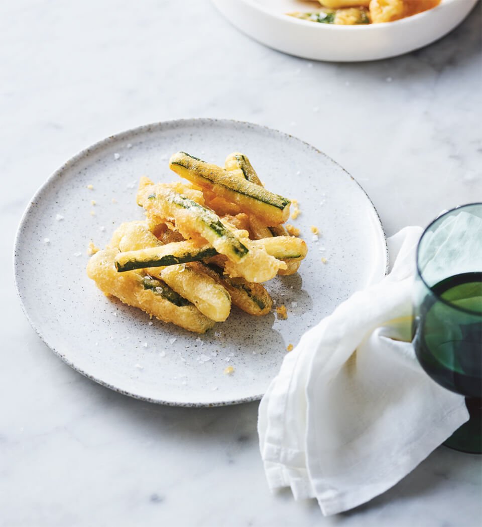 A white dish on a marble background with deep fried zucchini slices