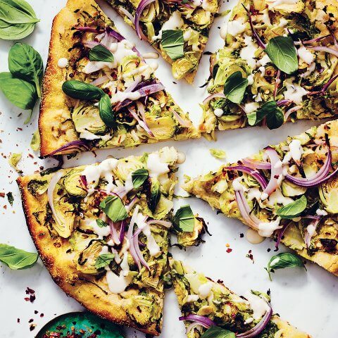 A sliced pizza topped with Brussels sprouts and other vegetables on a white surface