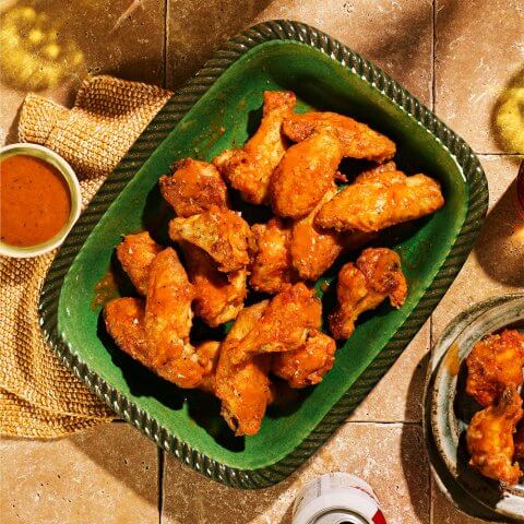 A green dish with chicken wings on a stone tabletop