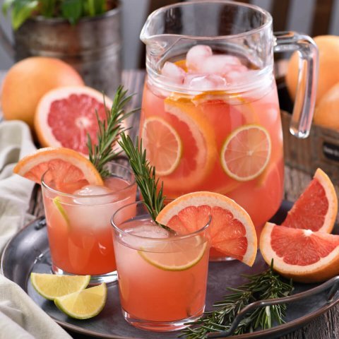 A pitcher full of ice and Paloma cocktails and surrounded by glasses of palomas.