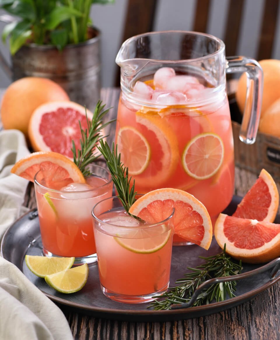 A pitcher full of ice and Paloma cocktails and surrounded by glasses of palomas.
