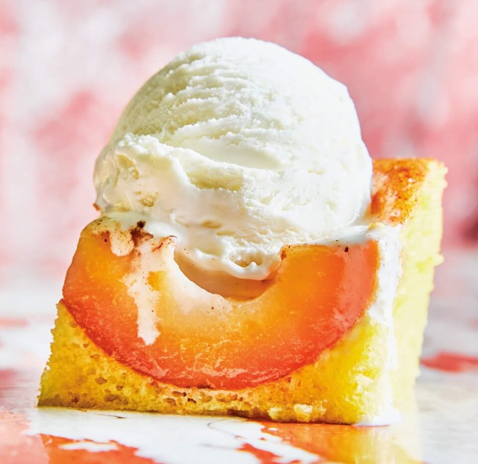 A slice of vanilla cake with a pear slice visible and a scoop of vanilla ice cream on top