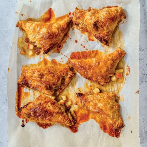 Six apple-stuffed pastries on a baking sheet covered with parchment paper