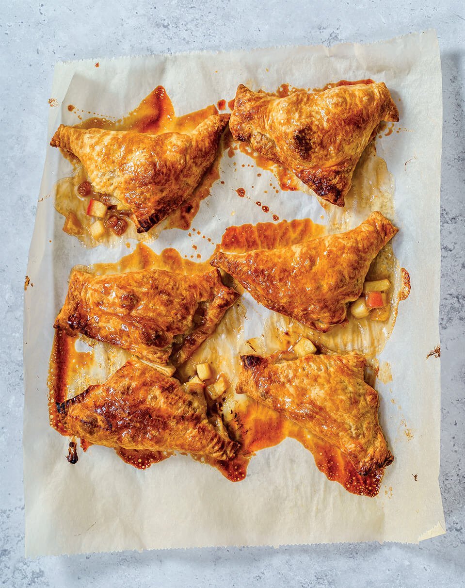 Six apple-stuffed pastries on a baking sheet covered with parchment paper