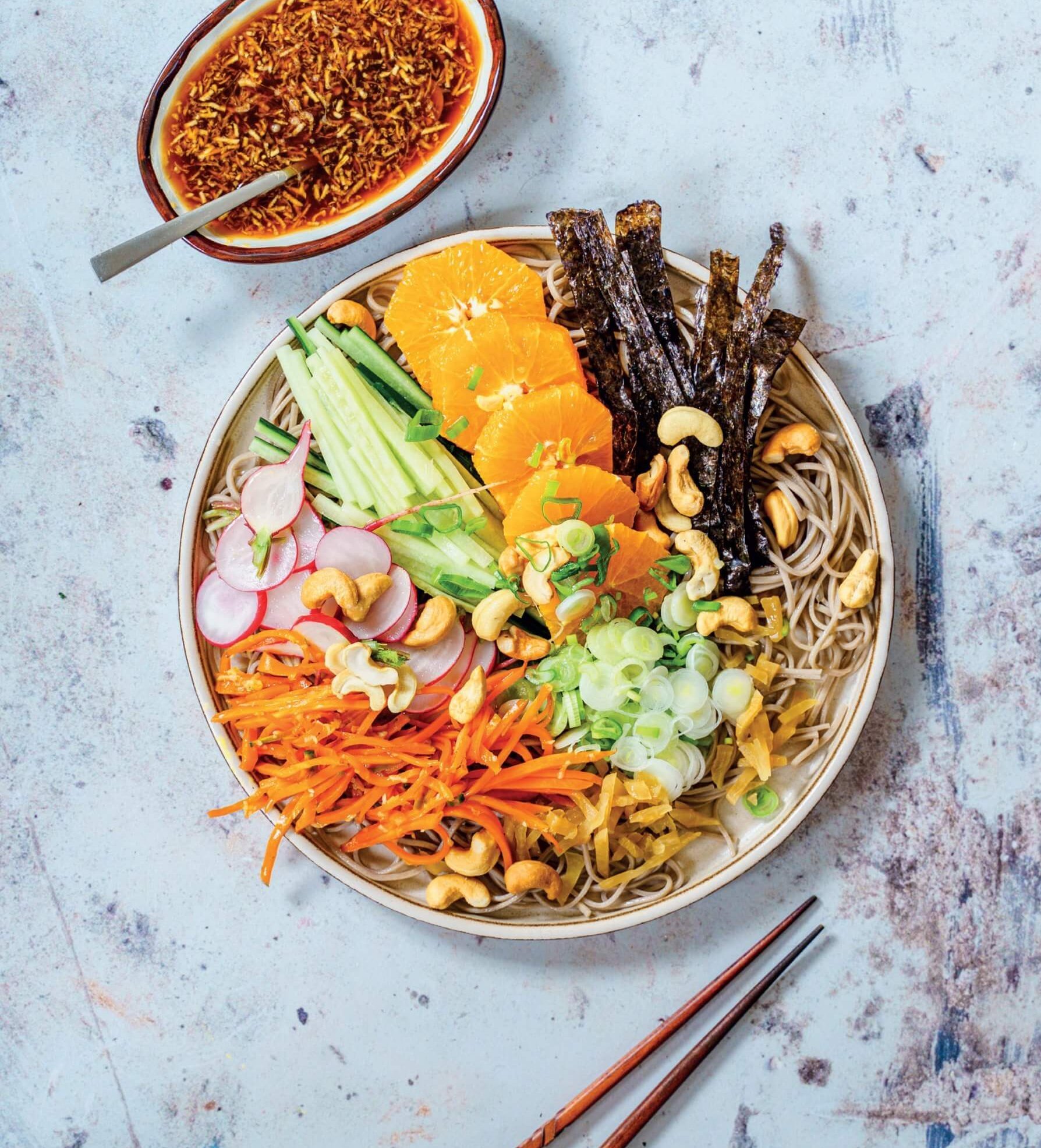 A bowl of salad with multicoloured ingredients, a dish of sauce and chopsticks