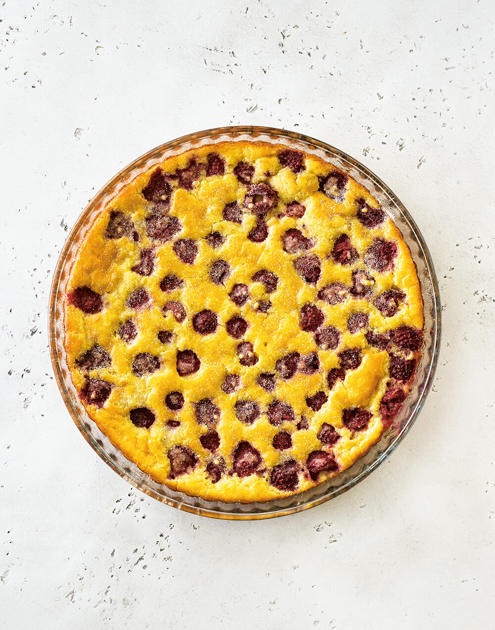 A yellow cake with raspberries on a white linoleum background