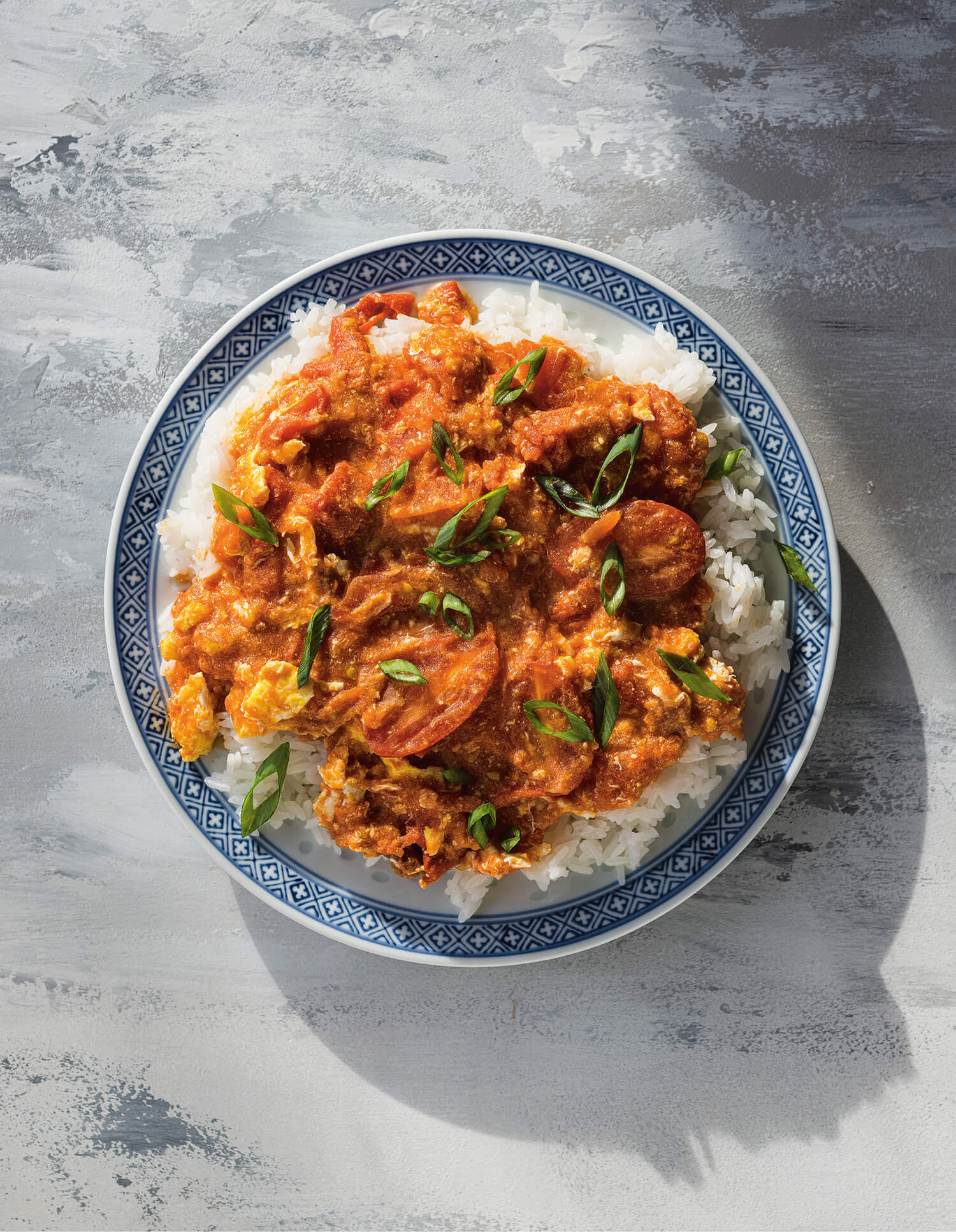 A blue dish with rice and a tomato-egg stir-fry on a grey surface