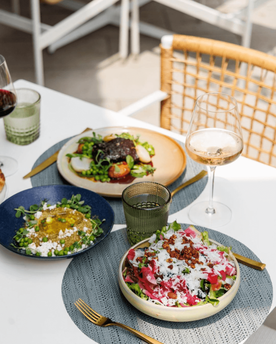 A patio table set with various dishes and a glass of white wine