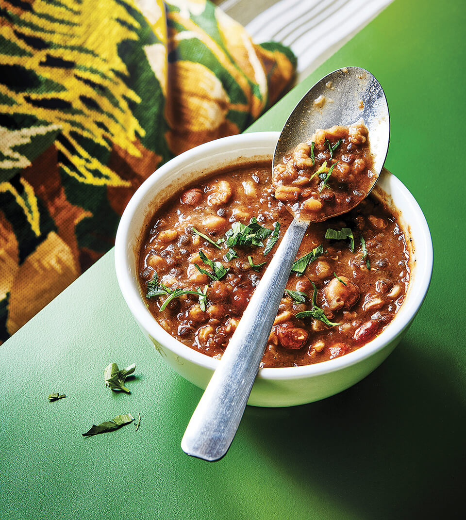 A bowl of soup on a bright green table with an embroidered pillow in the background
