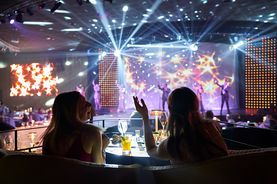 Two women at a dining table watching a show with multicoloured strobe lights