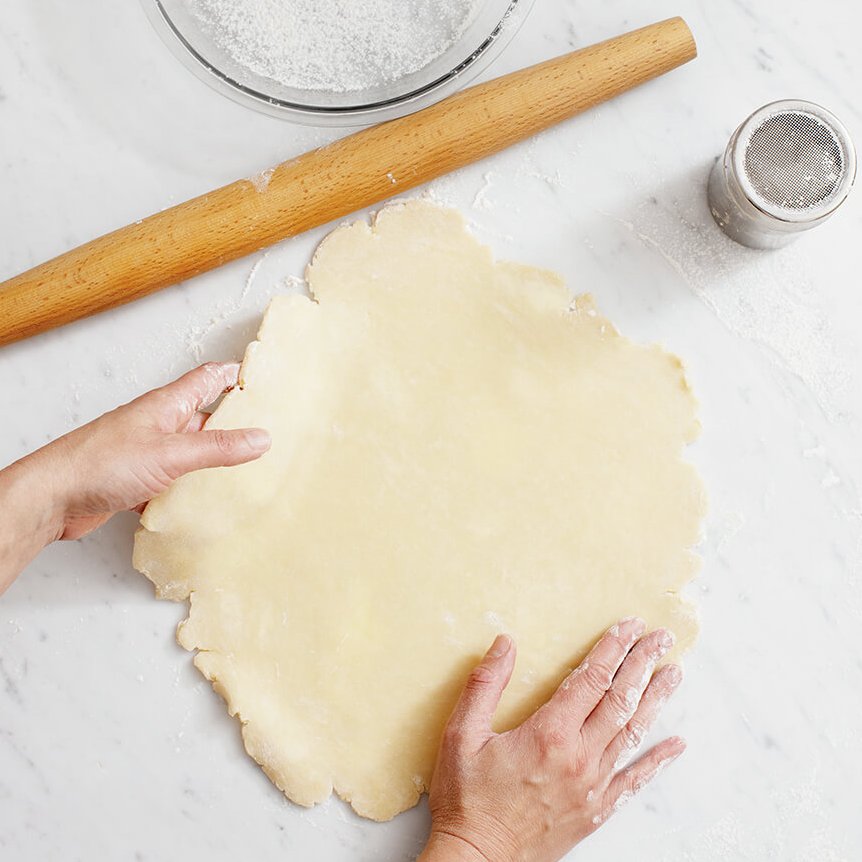 Anna Olson rolling out her classic pie dough recipe on a white marble surface