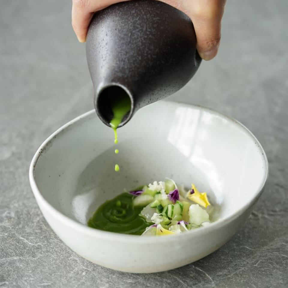 A person pouring green sauce into a white bowl