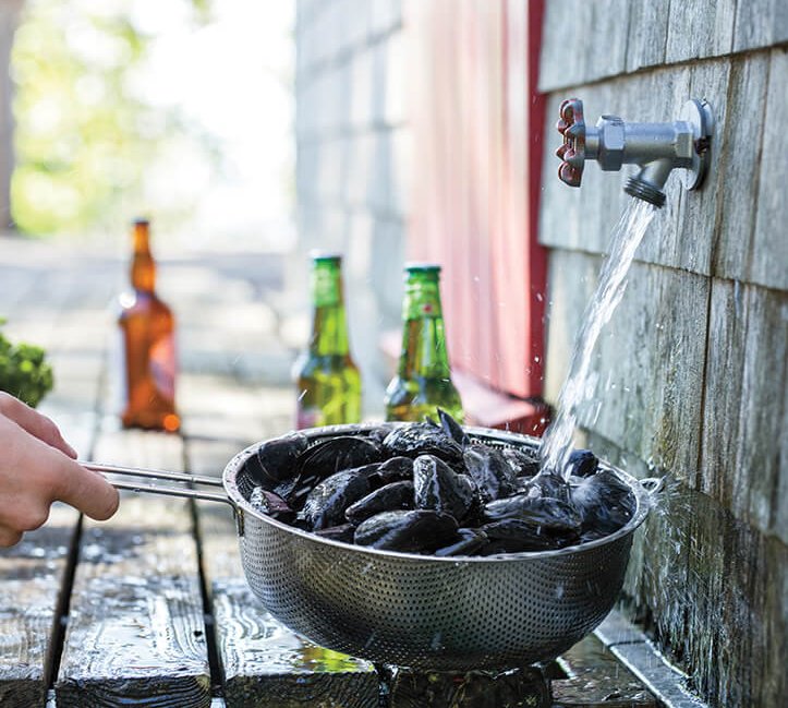 A person rinsing mussels in a sieve at an outdoor tap