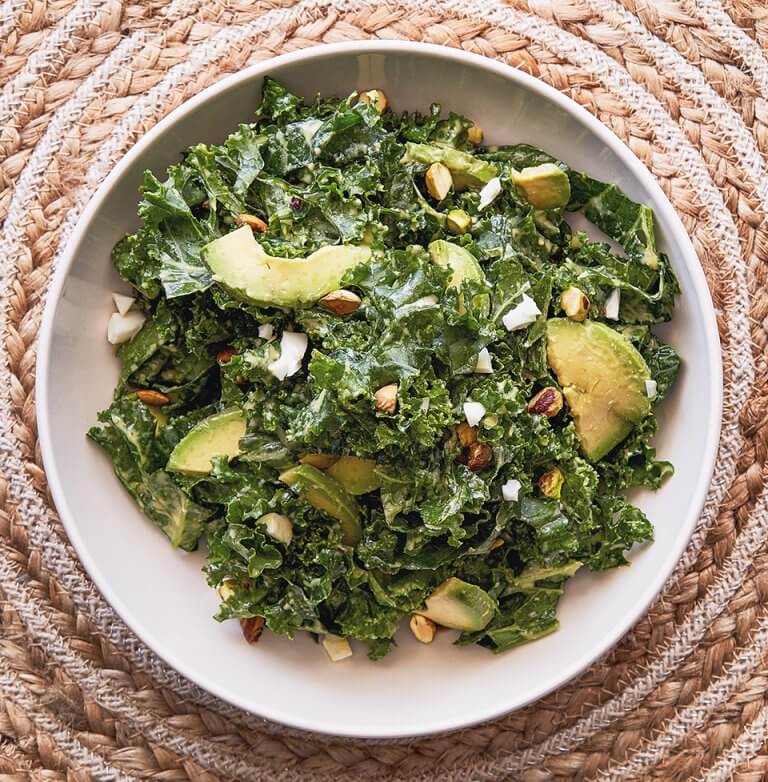 A bowl of kale salad on a woven wicker trivet