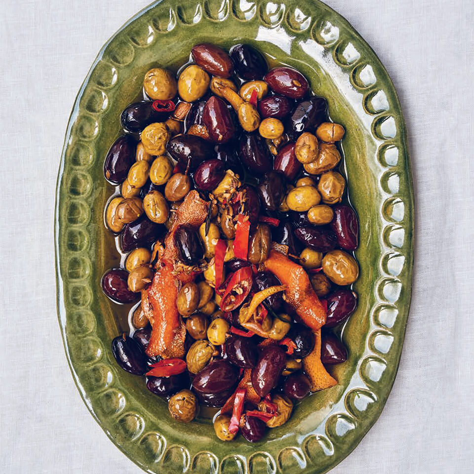 A green dish with mixed olives on a white tablecloth